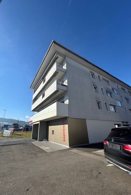 4 story apartment building, with a garage entrance on the ground floor, located on a busy road with a parking lot