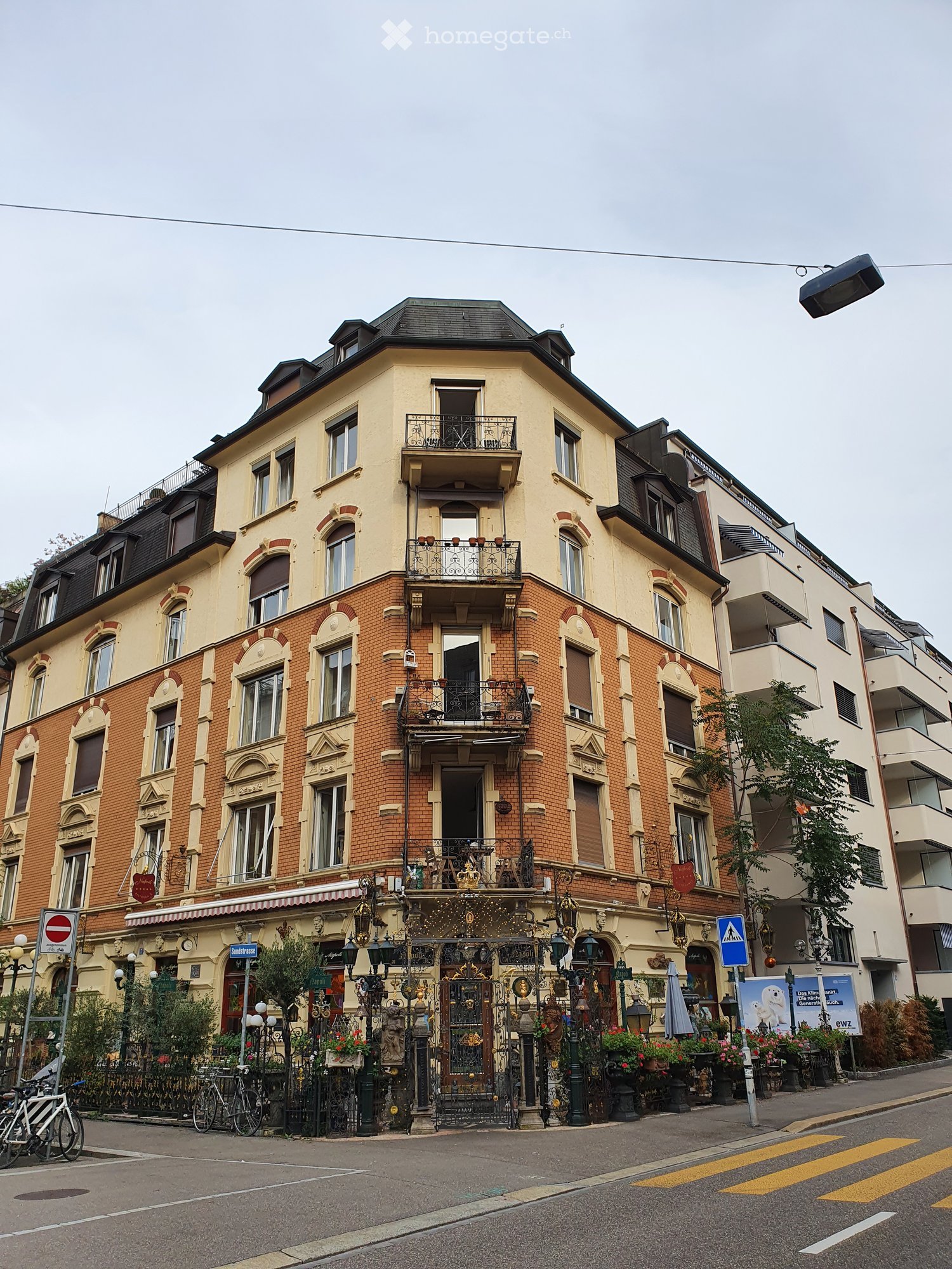 A multi-story residential building with ornate balconies, brick and plaster facade, decorative street-level storefront, and bicycles parked nearby.