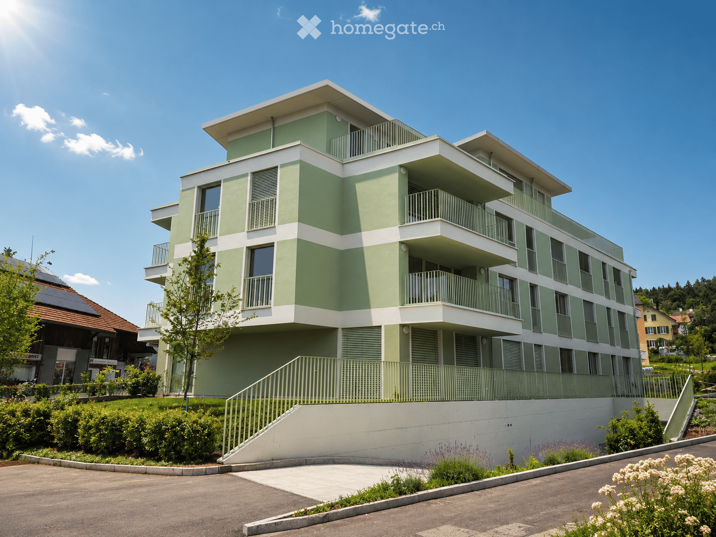 Modern three-story residential building with green and white exterior, multiple balconies, and a raised ground floor entrance.