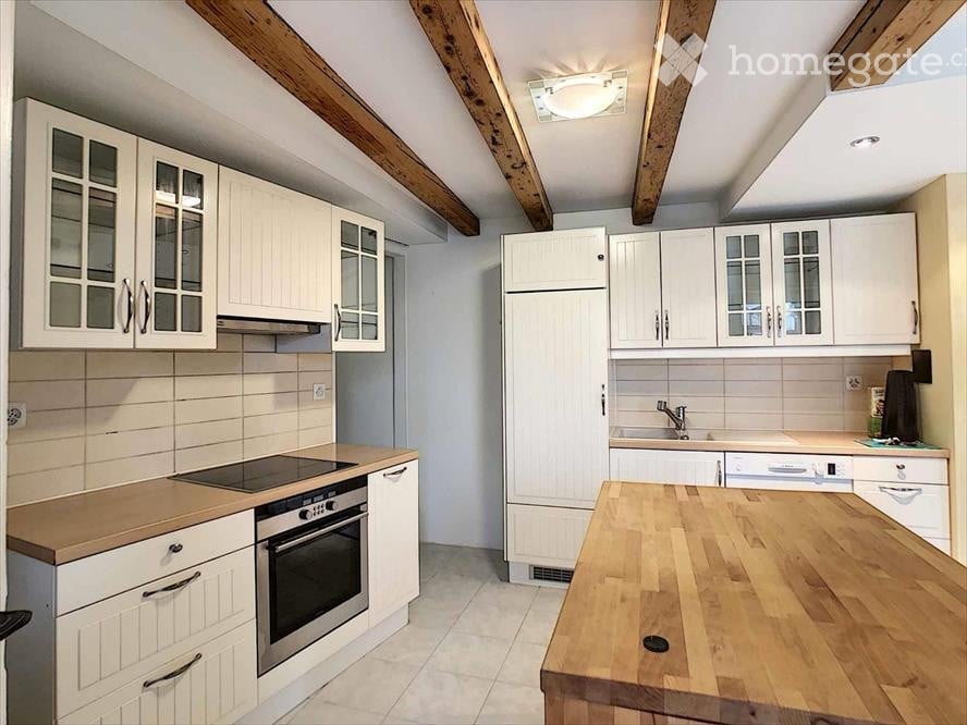 Bright kitchen with white cabinets, wooden countertops, and stainless steel appliances including a refrigerator, oven, and dishwasher. Exposed wooden beams on the ceiling.