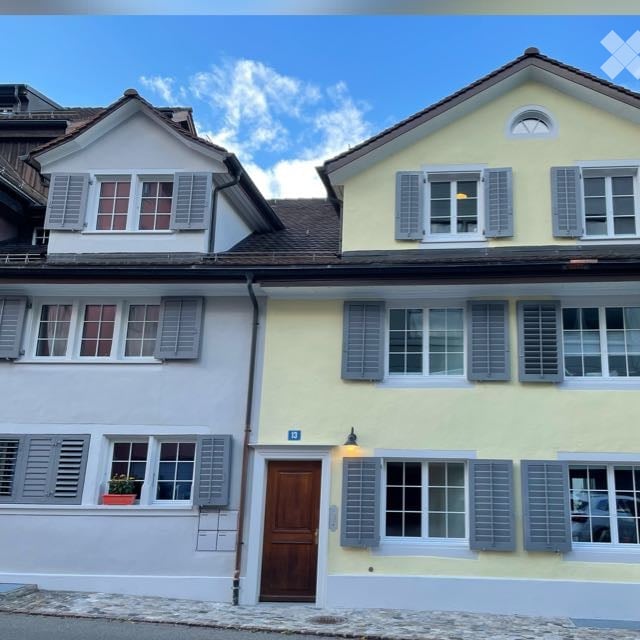 Two-story residential building with white and yellow facades, multiple windows with shutters, and a wooden front door.