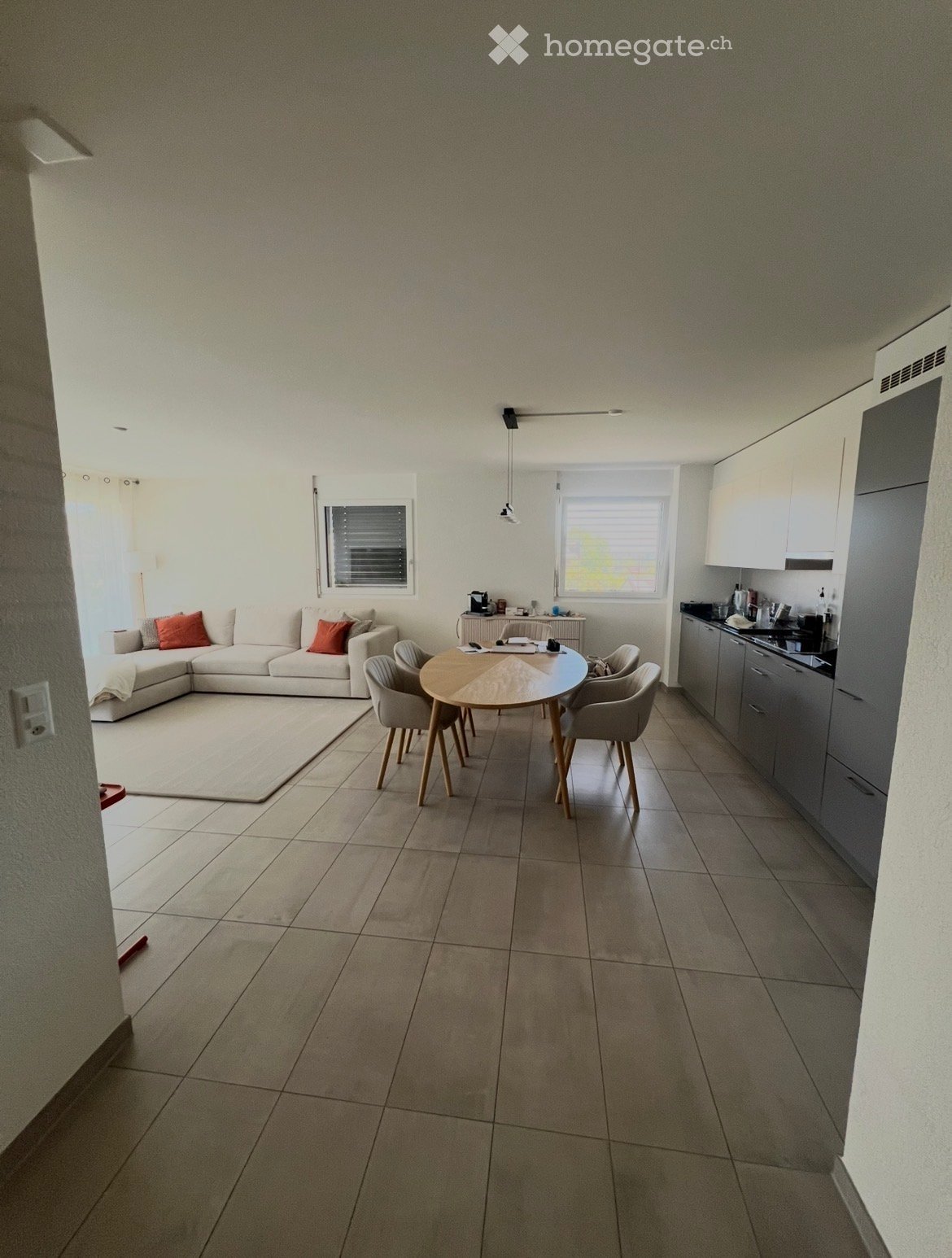 Open-plan living and dining area with a sofa, dining table, chairs, and a kitchen area with cabinets and a counter.