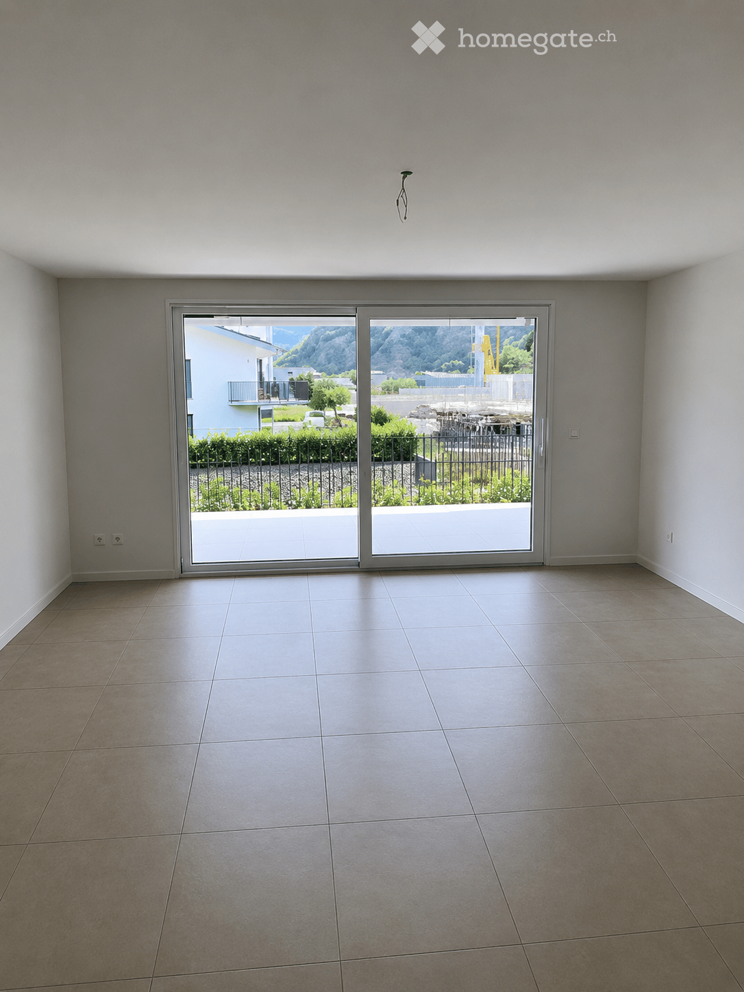 Empty room with tiled floor, large sliding glass doors leading to a balcony or outdoor area, and neutral-colored walls.