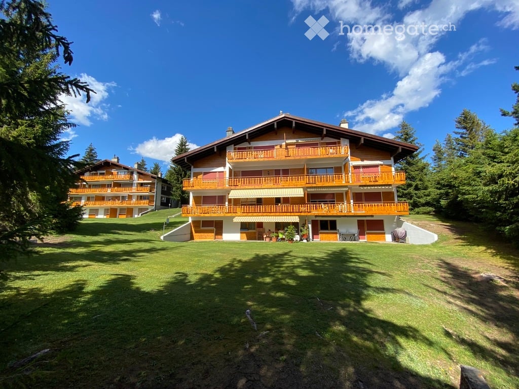 A large, multi-story wooden building with balconies and a well-maintained lawn in a forested area.