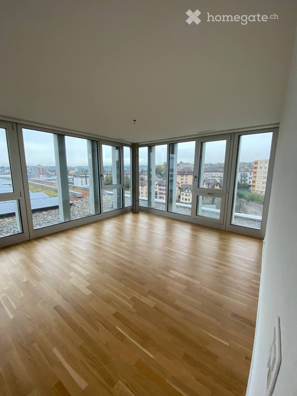 Completely empty room with wooden flooring and large windows offering a cityscape view.
