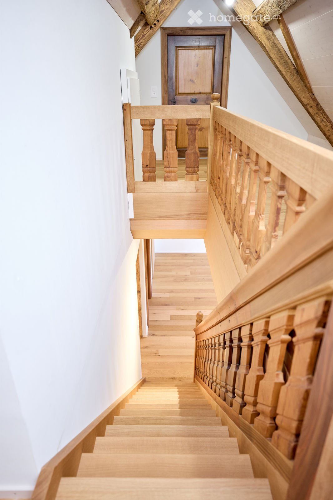 Wooden staircase with a handrail and balusters, leading to a closed wooden door at the top.