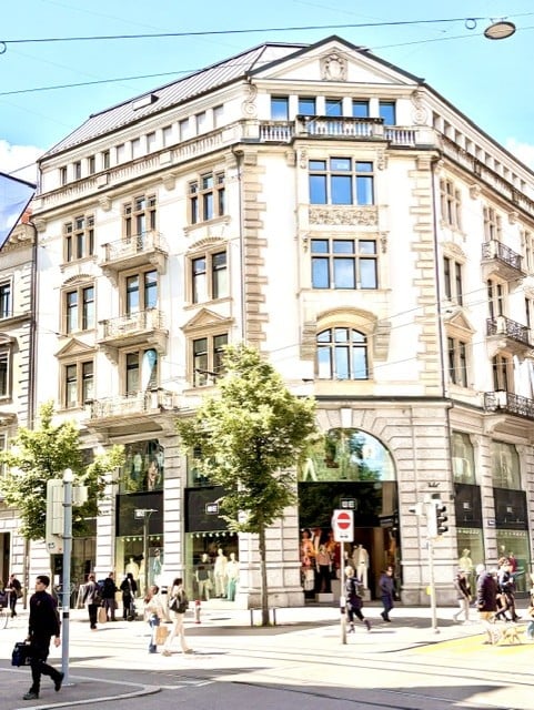 A multi-story building with classic architectural details, large windows, and balconies. The ground floor features retail storefronts with glass windows and doors.