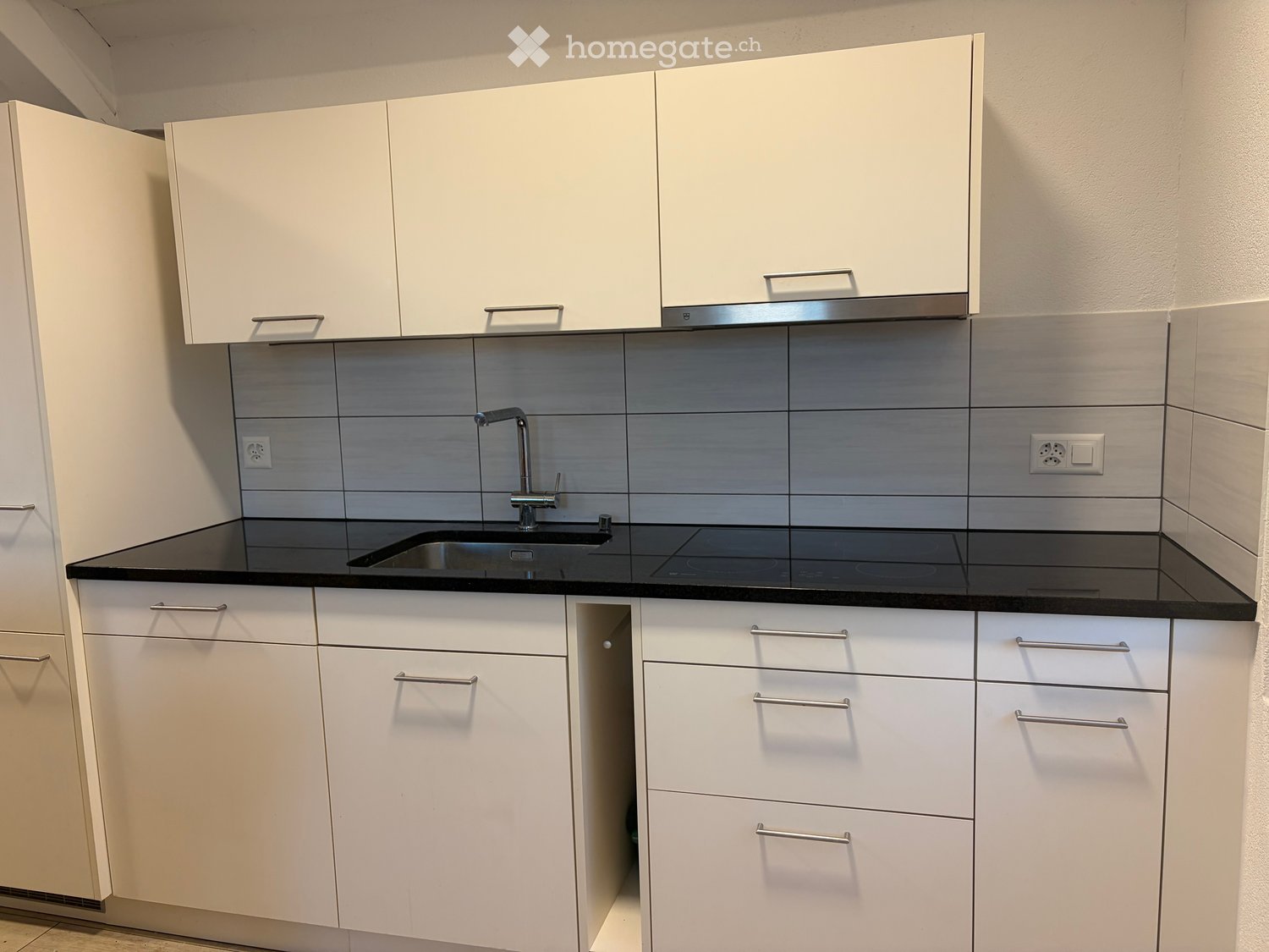 Modern kitchen with white cabinets, black countertop, stainless steel sink, and faucet.