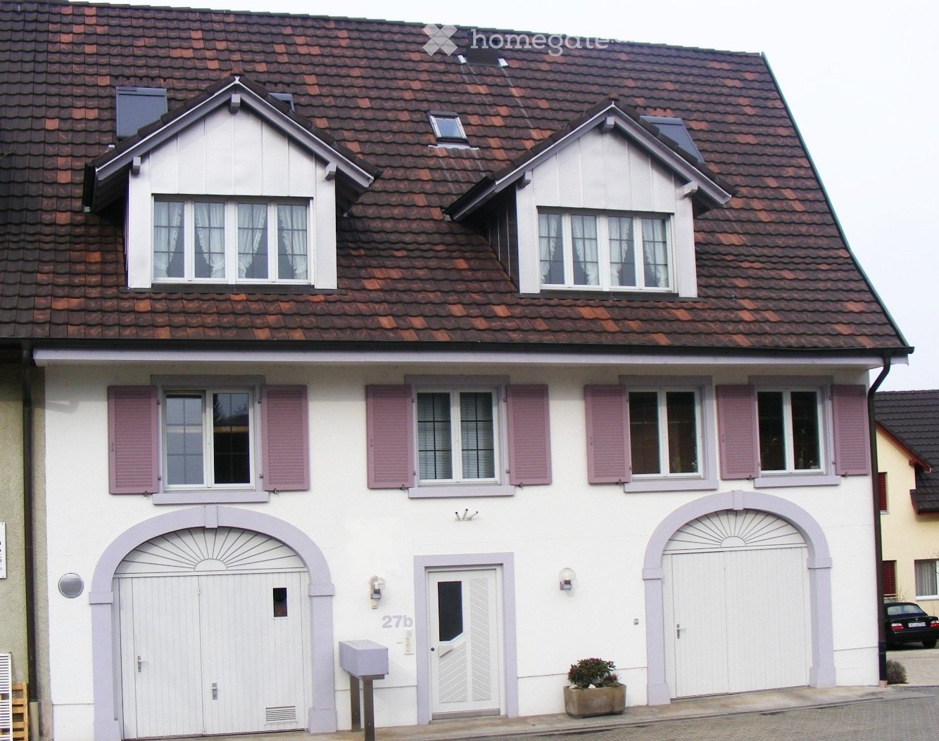 Two-story house with white exterior, red-tiled roof, multiple windows with pink shutters, and a garage entrance.
