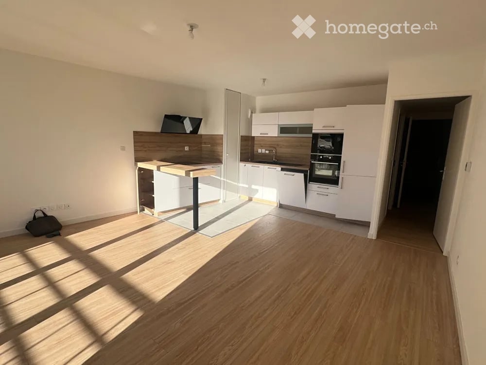 Modern kitchen with white cabinets, wooden countertop, built-in oven, dishwasher, and a screen on the counter. Light wooden flooring and bright lighting.