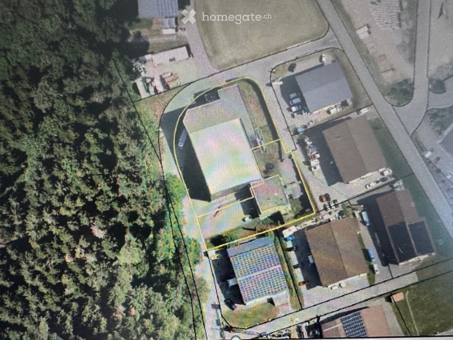 Aerial view of a residential property with multiple buildings, including a main house, garage, and outbuildings, surrounded by trees and a driveway.