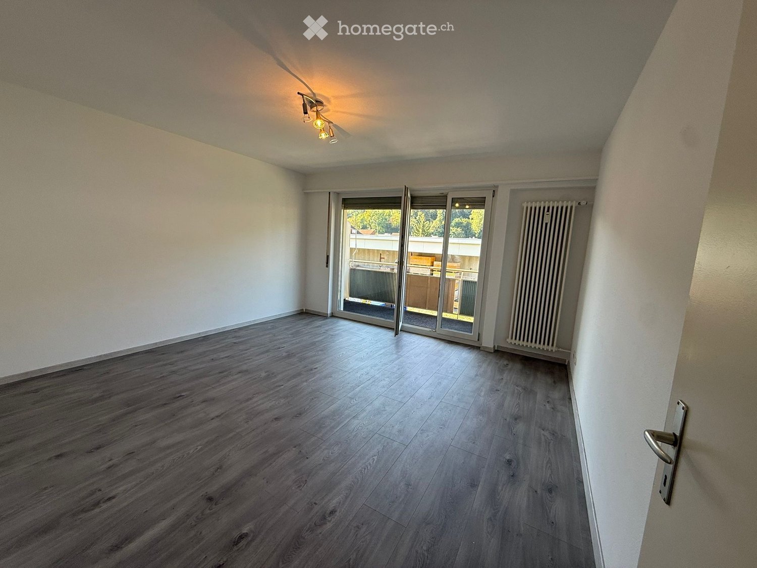 Empty room with wooden flooring, white walls, and a sliding glass door leading to a balcony area.
