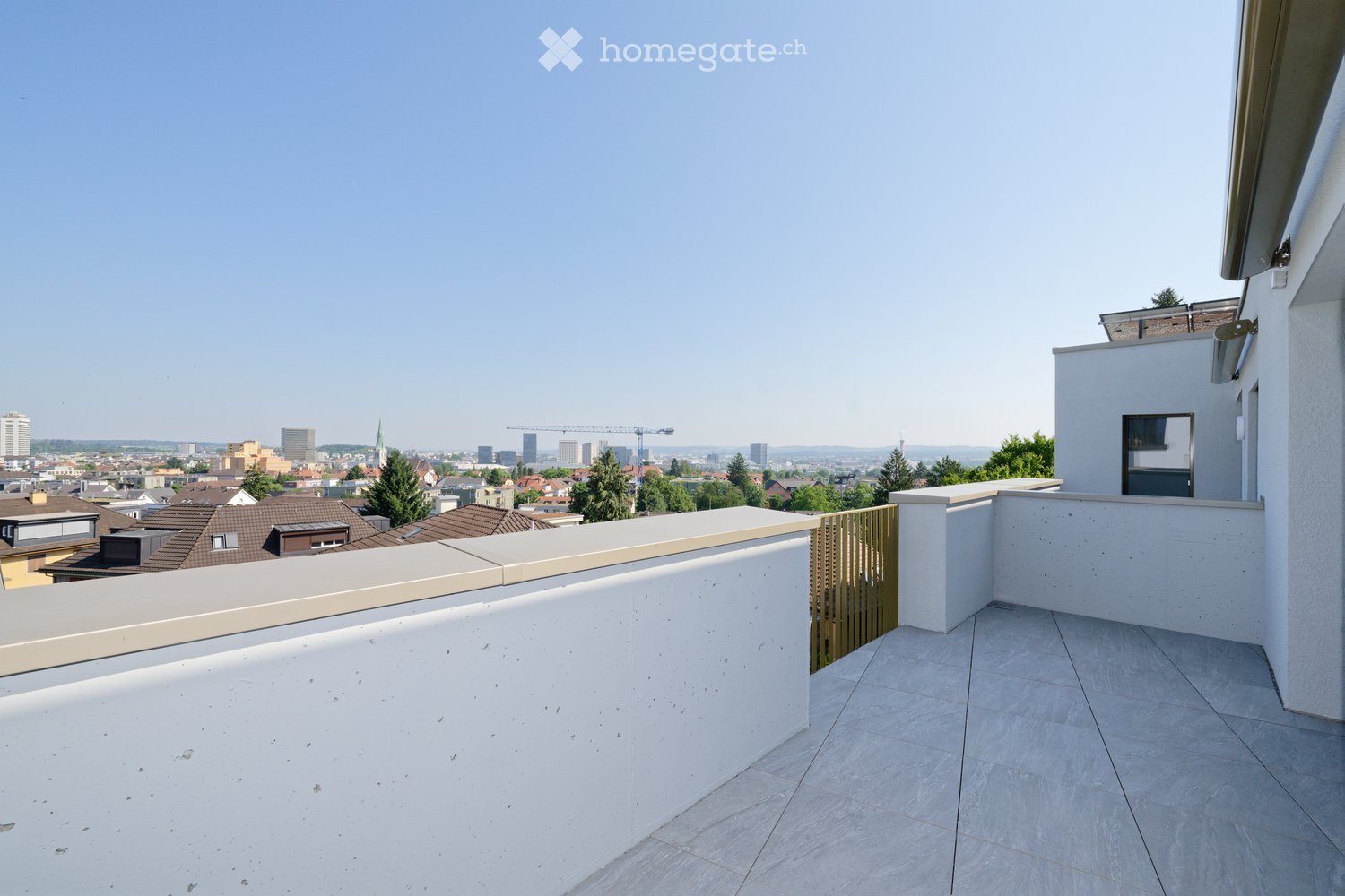 Modern rooftop terrace with tiled flooring, white low wall, and metal railing, offering panoramic cityscape view.
