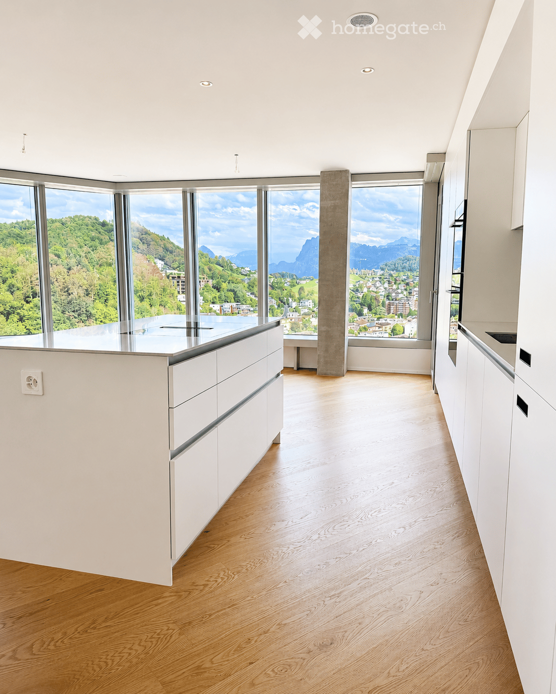 Modern, minimalist kitchen with white cabinets, a central island, and large windows offering a scenic mountain view.