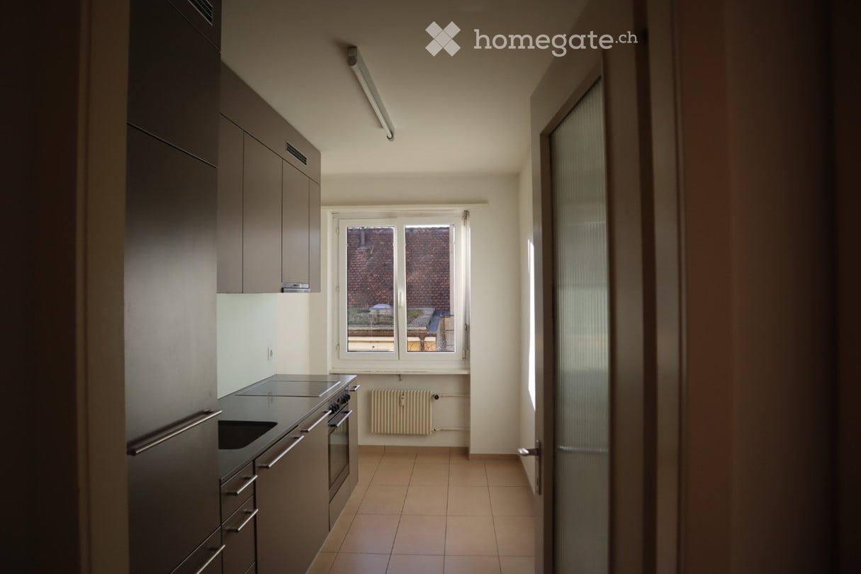 Modern kitchen with dark cabinets, stainless steel appliances, tiled floor, and a window overlooking a courtyard.