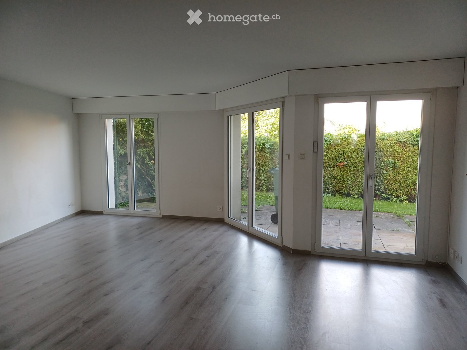 Empty room with light wooden flooring and large sliding glass doors leading to an outdoor area.