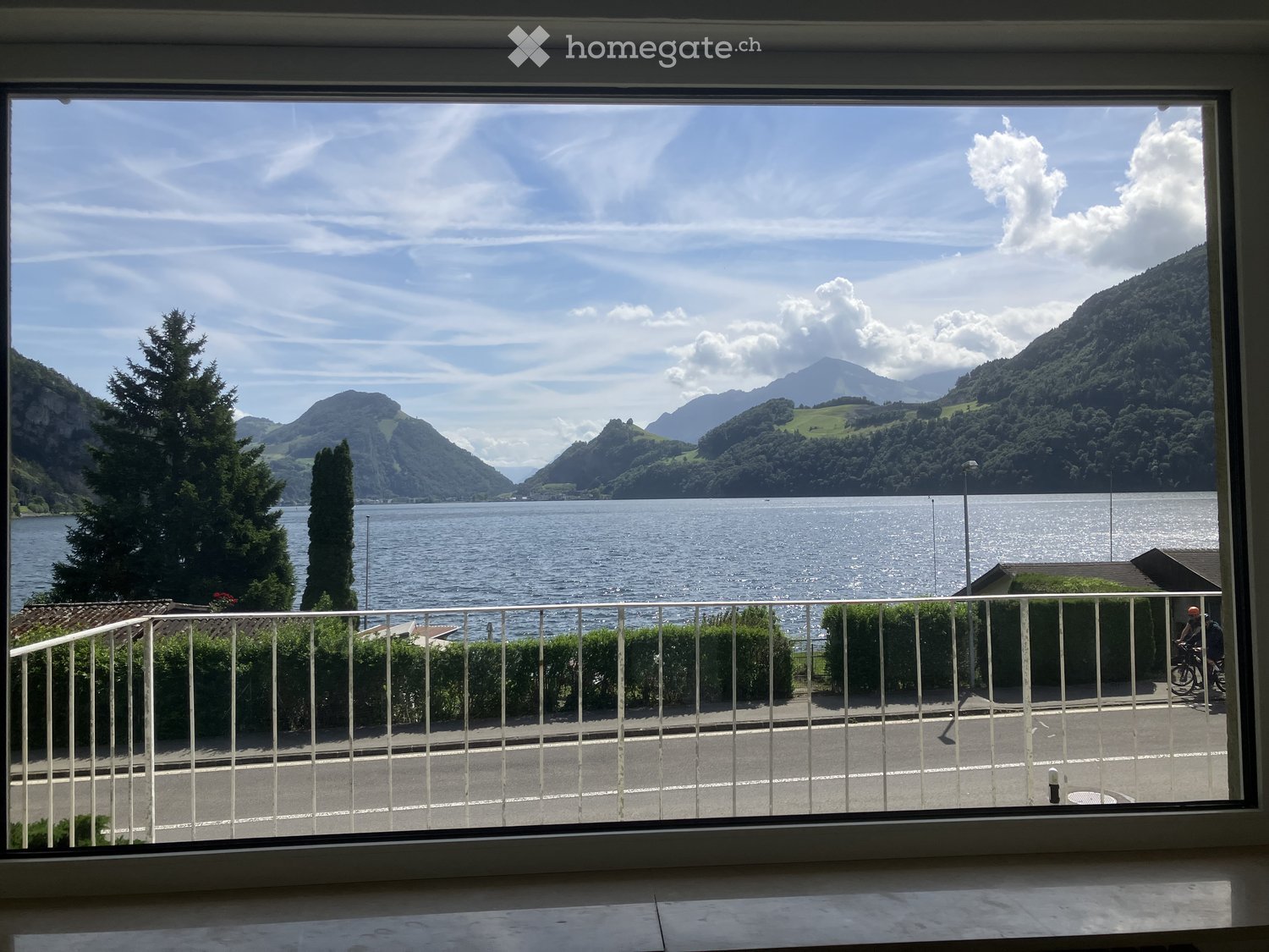 Balcony overlooking a scenic lake and mountain landscape with a clear blue sky and scattered clouds.