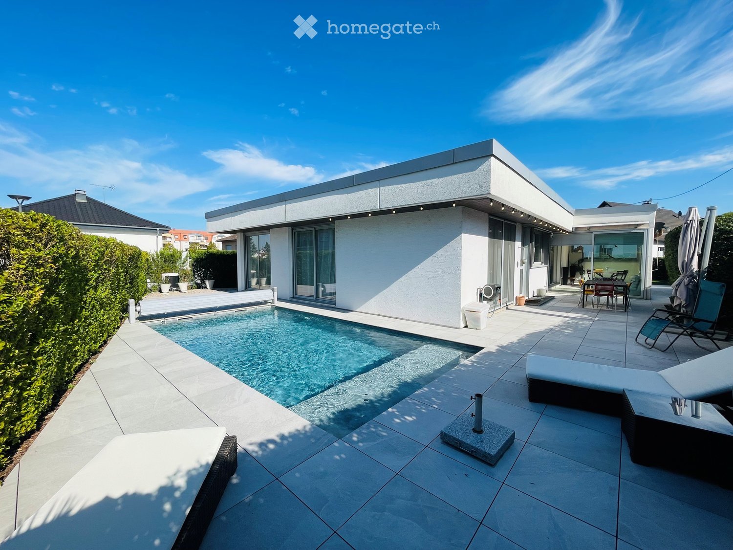 Modern outdoor area with a swimming pool, sun loungers, and a dining set near the house.