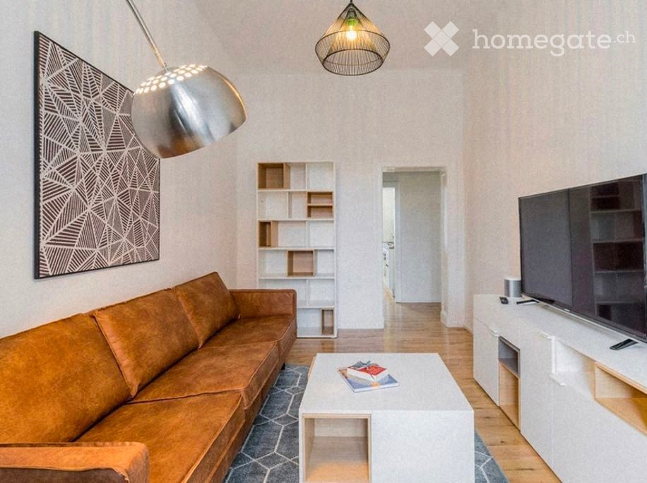 Modern living room with a brown leather sofa, white coffee table, bookshelf, TV stand, and decorative wall art.