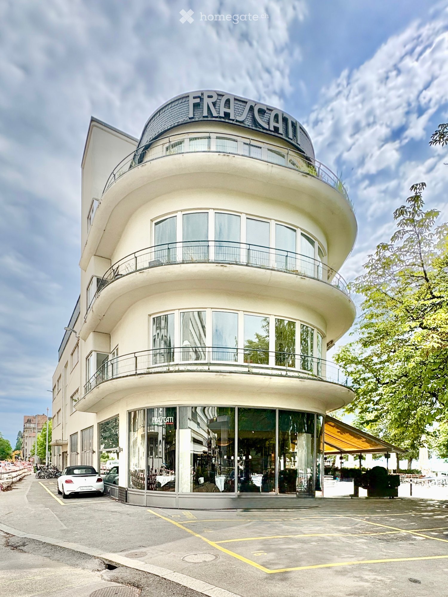 Modern, curved building with large glass windows and balconies, featuring the sign "FRASCATI" on the roof.
