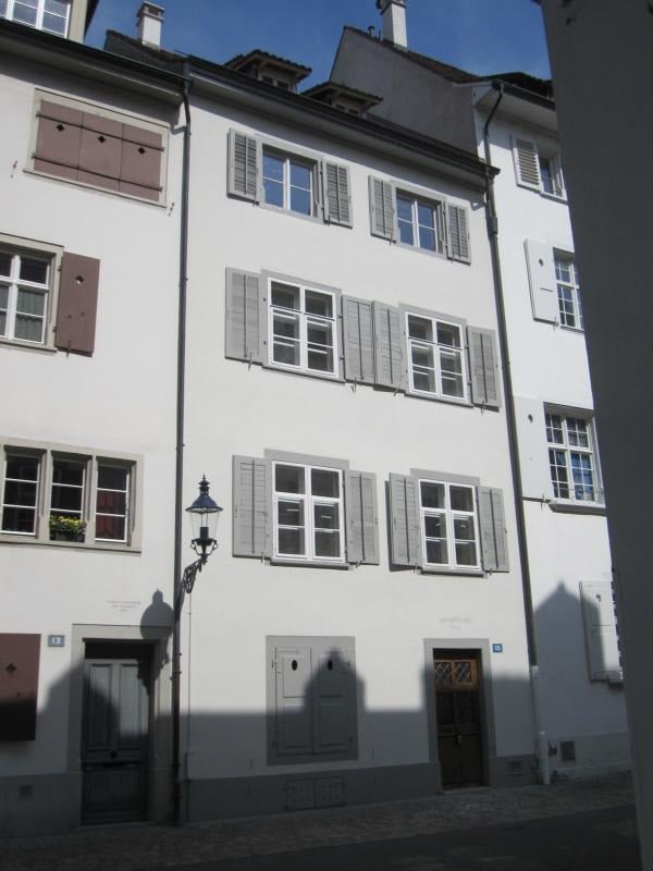 A multi-story white building with multiple windows, shutters, and doors. The building has a classic architectural style with a clean facade and a street lamp in front.
