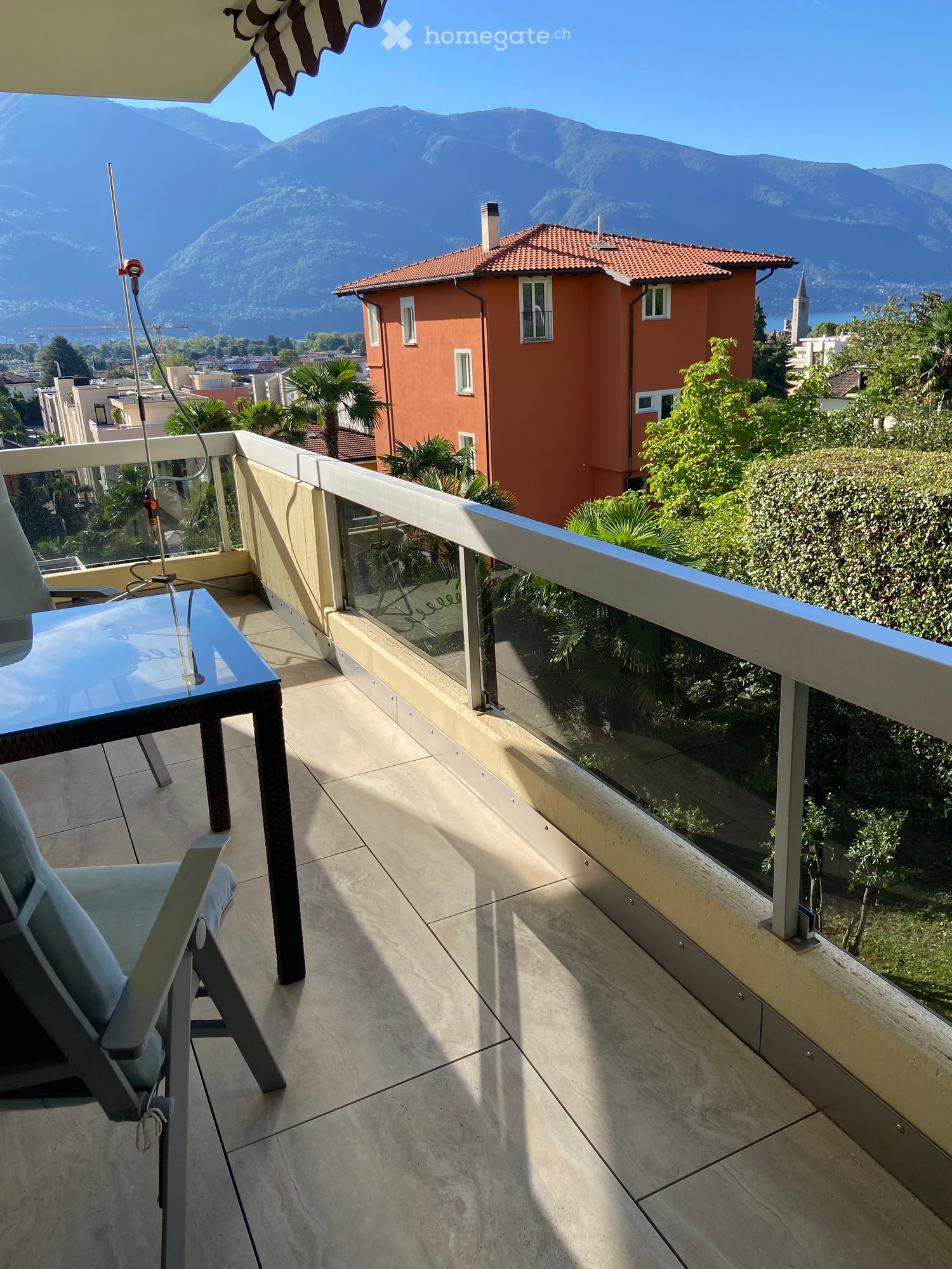 Balcony with a view of mountains and a lake, featuring a table and a chair.