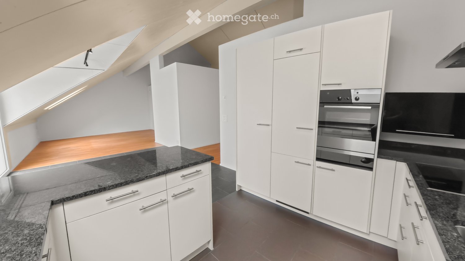 Modern kitchen with white cabinets, granite countertops, and stainless steel oven. Wooden flooring in part of the space.