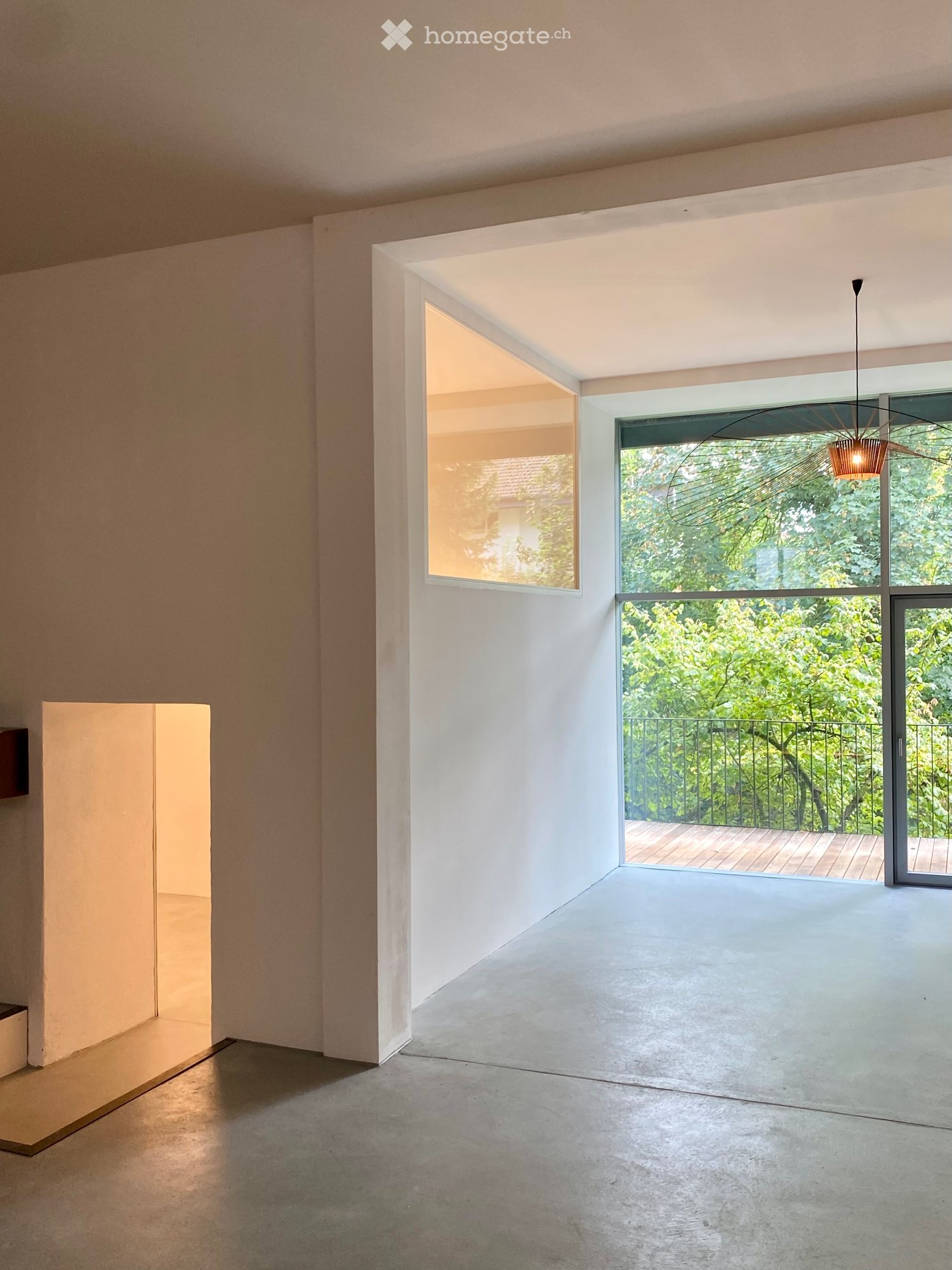 Empty room with large windows and a view of greenery, featuring a modern, minimalist design with concrete floors and white walls.