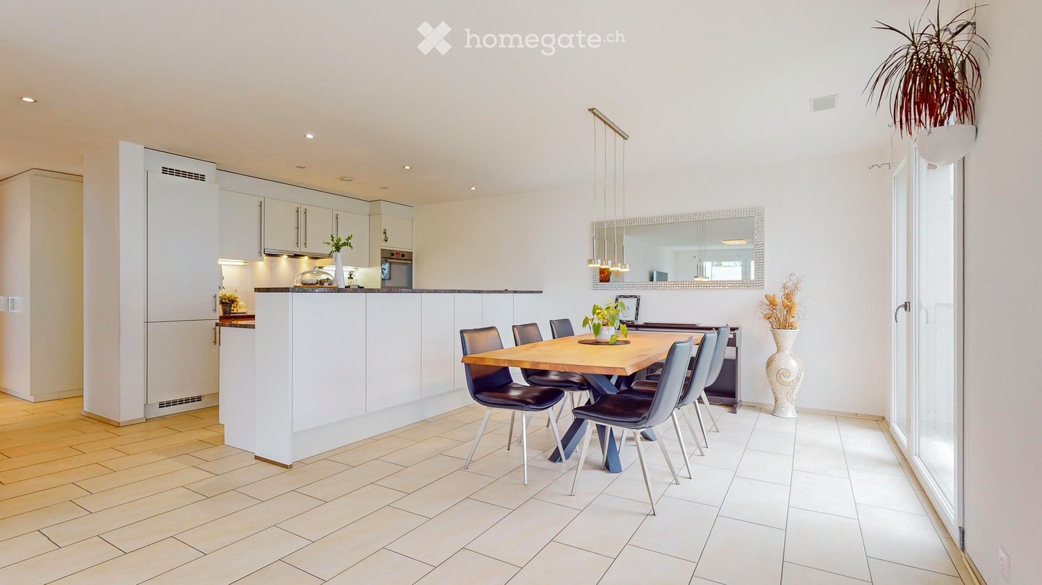 Modern kitchen and dining area with white cabinets, a wooden dining table, six chairs, and a large mirror above the counter.