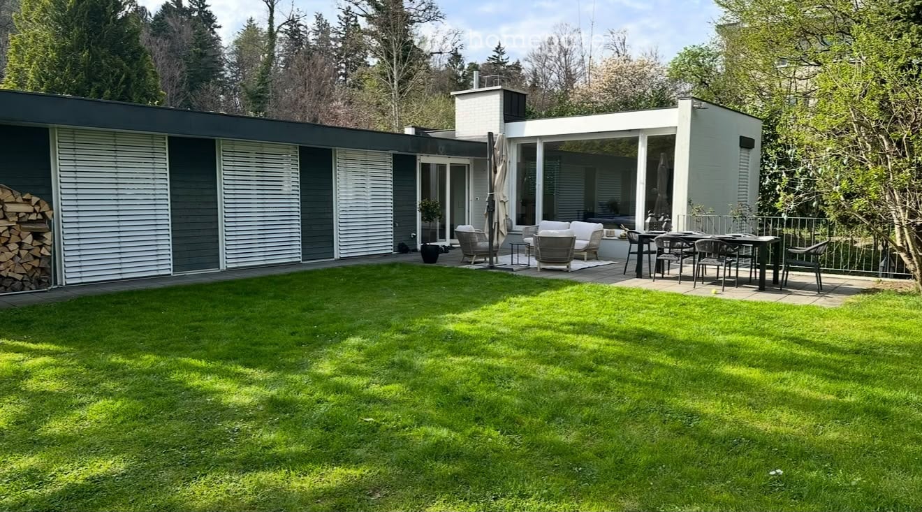 Modern house with a spacious garden, patio seating area, and outdoor dining set.