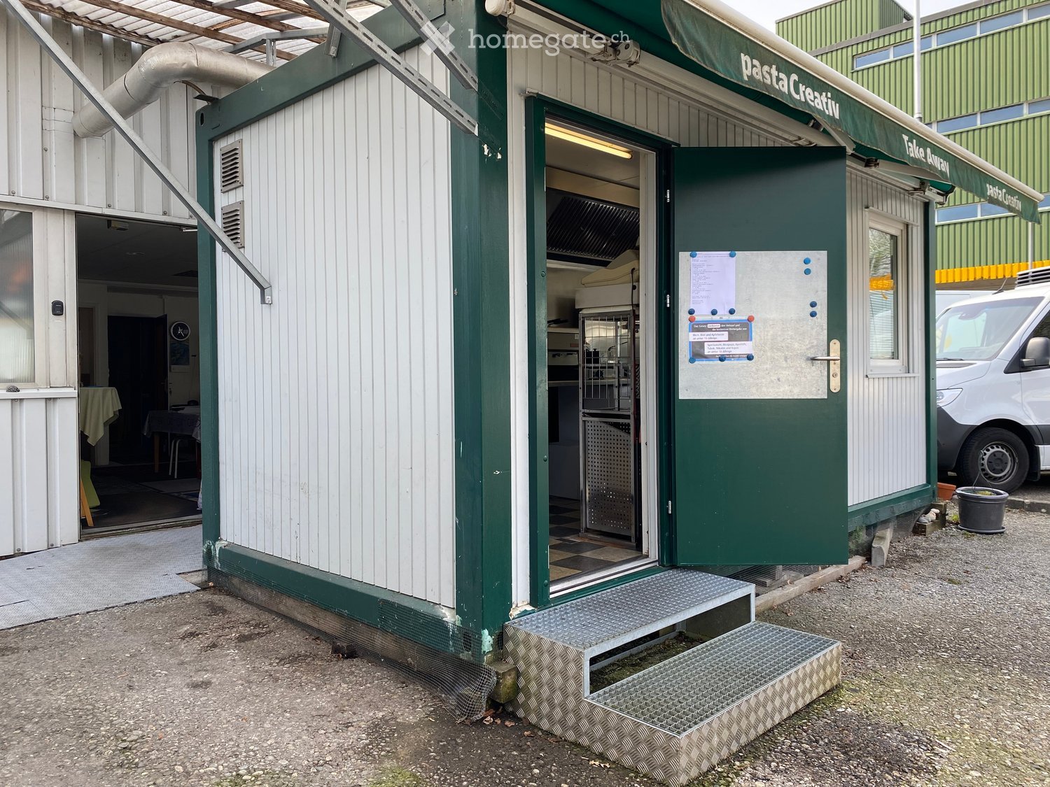 A small, green and white building with a green awning labeled "Pasta Creativa" and a "Take Away" sign. The entrance has a metal ramp and steps, with a partially visible interior showing kitchen equipment and a dining area.