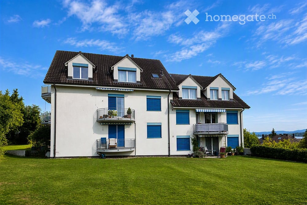 Two-story white house with blue shutters, multiple balconies, and a well-maintained lawn.