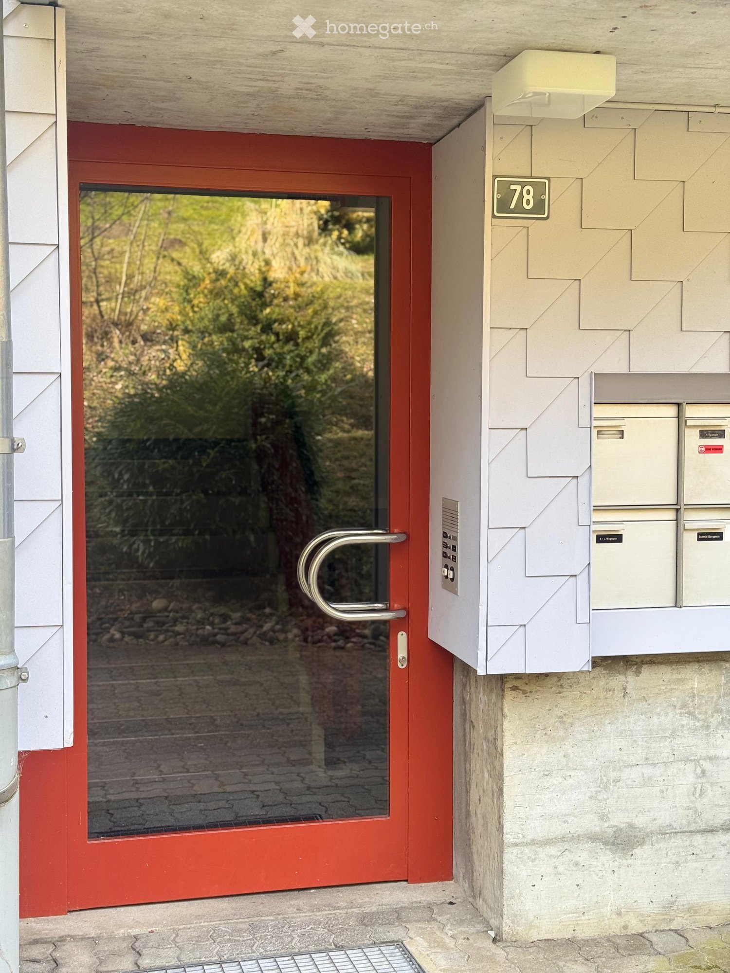 Entrance to a building with a red door, glass panel, and mailboxes on the wall.