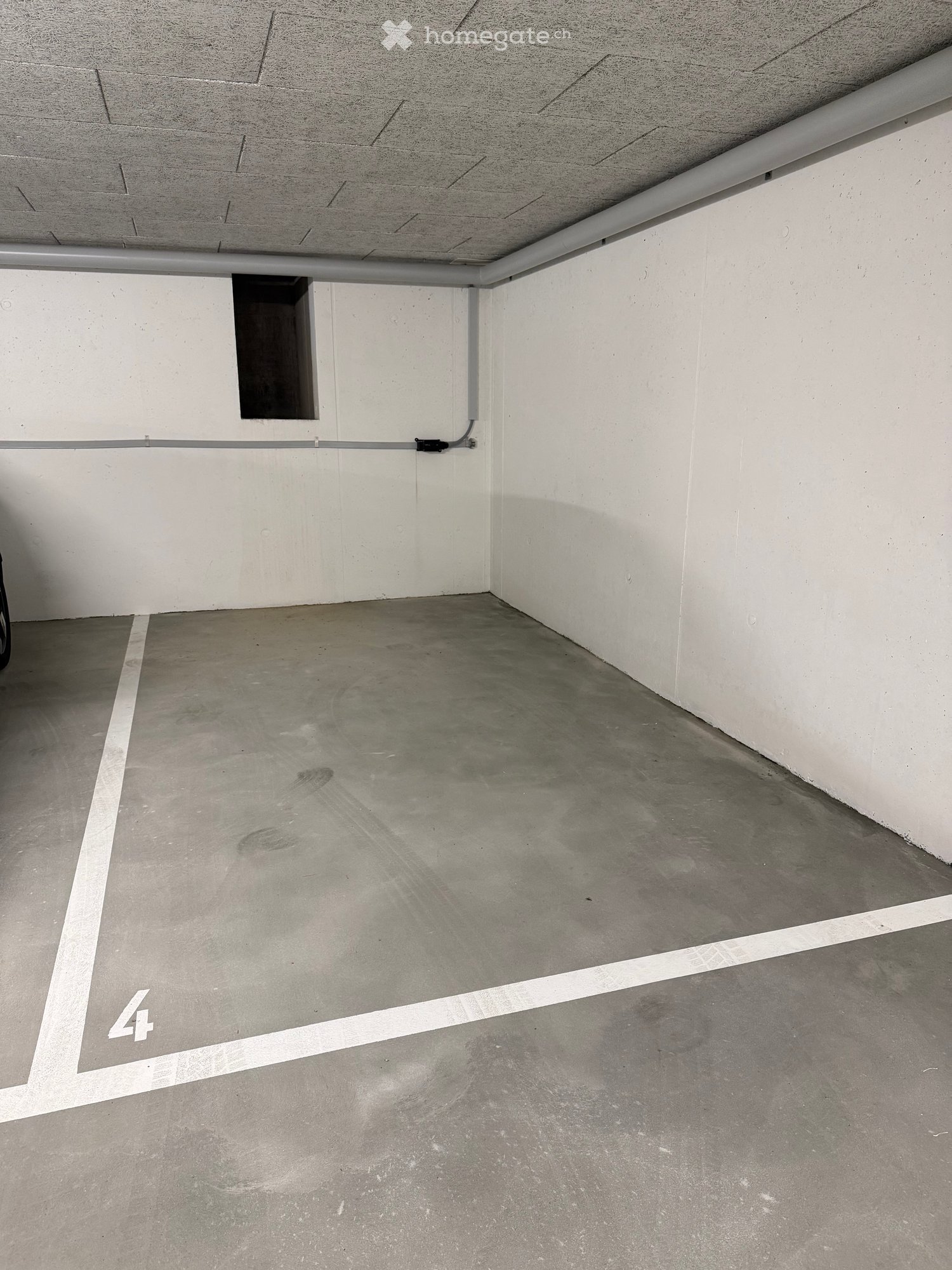 Empty underground parking space with concrete floor and white walls, marked with number '4'.