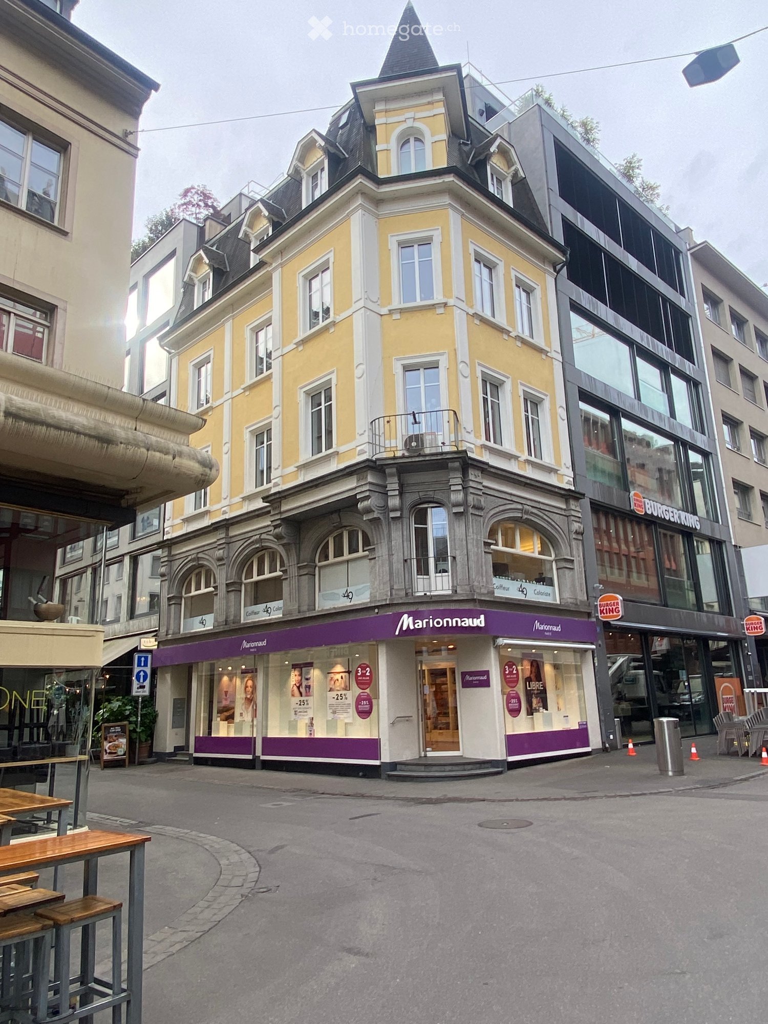 Multi-story building with yellow facade, arched windows, and a purple storefront for Marionnaud. Adjacent buildings include a Burger King and other commercial spaces.