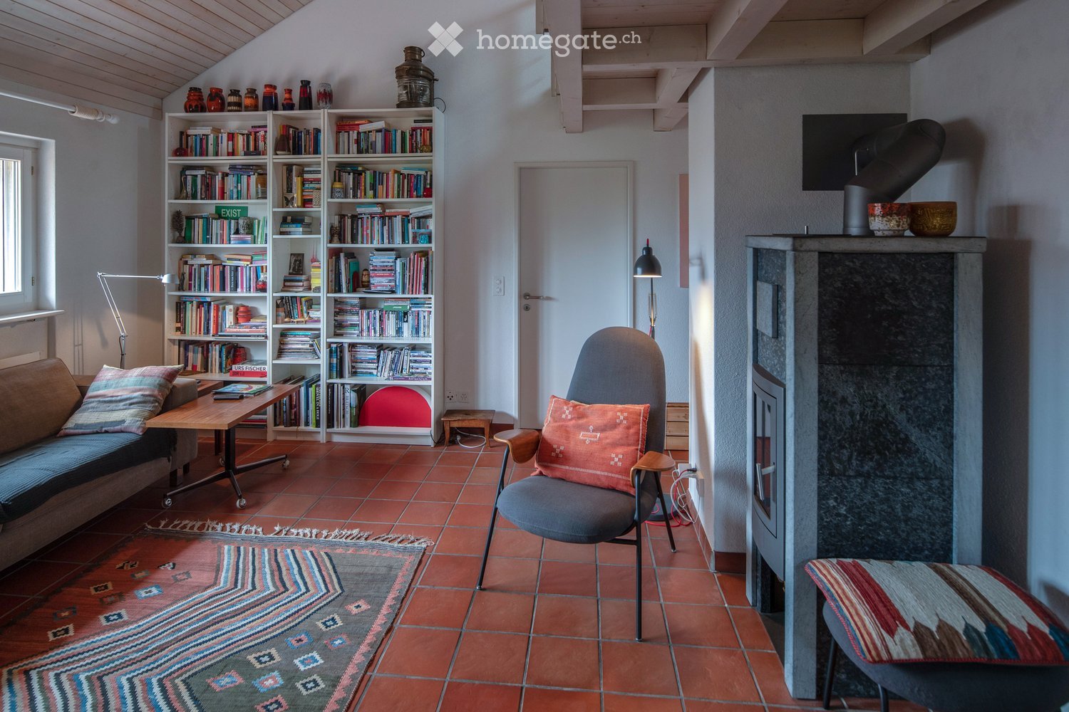 Living room with a fireplace, bookshelf, sofa, chair, table, and a television mounted on the wall.