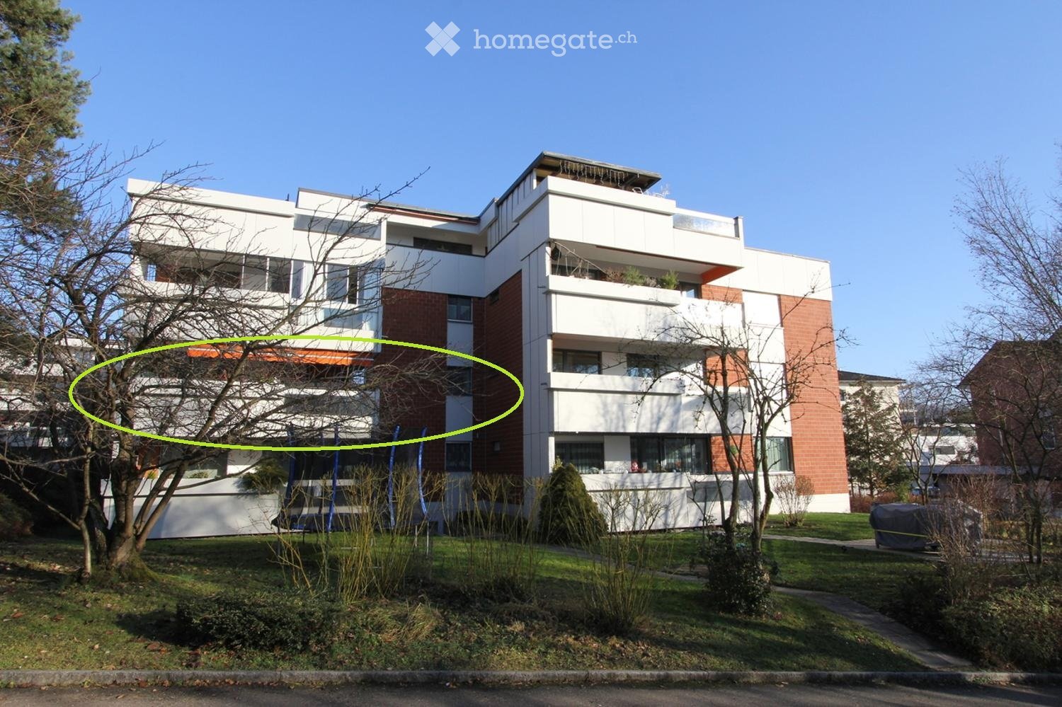 Modern multi-story residential building with white and red brick facade, multiple balconies, and surrounding greenery.