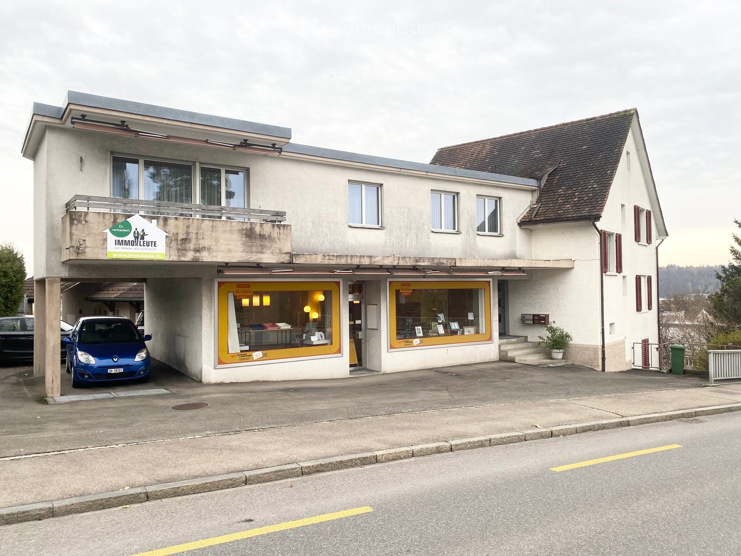 Two-story building with a garage, storefronts, and a balcony on the upper level.