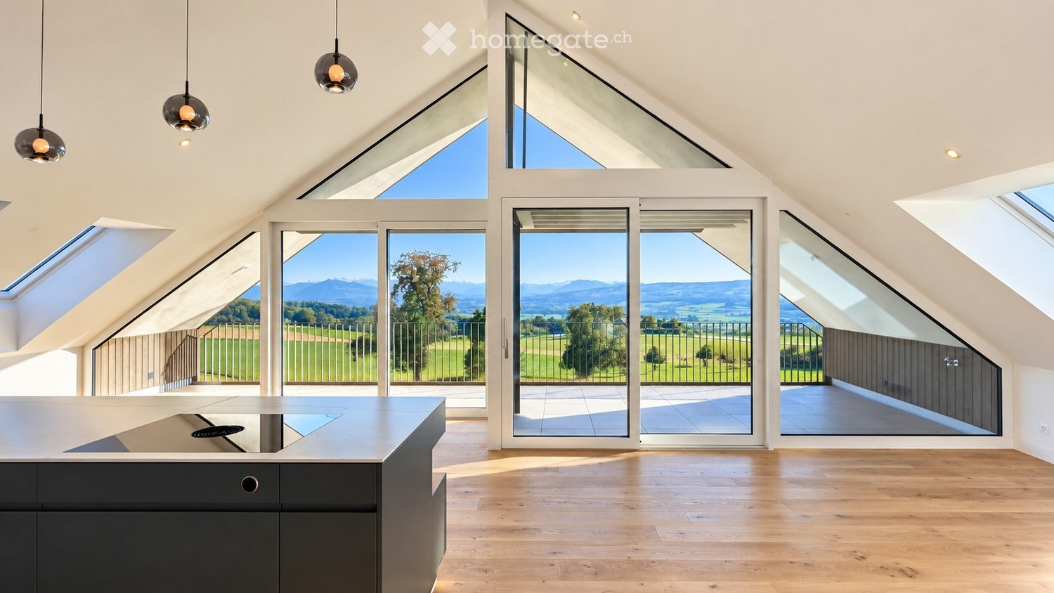 Modern kitchen with wooden flooring, sleek black kitchen island, large windows offering scenic views, and pendant lights.