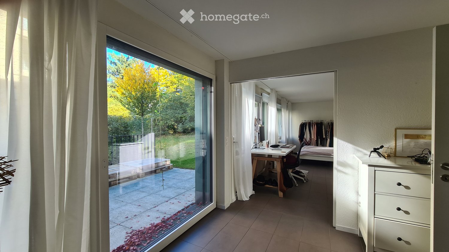 Bright, modern room with large glass sliding doors leading to a patio, a desk with a chair, a bed, and a wardrobe.