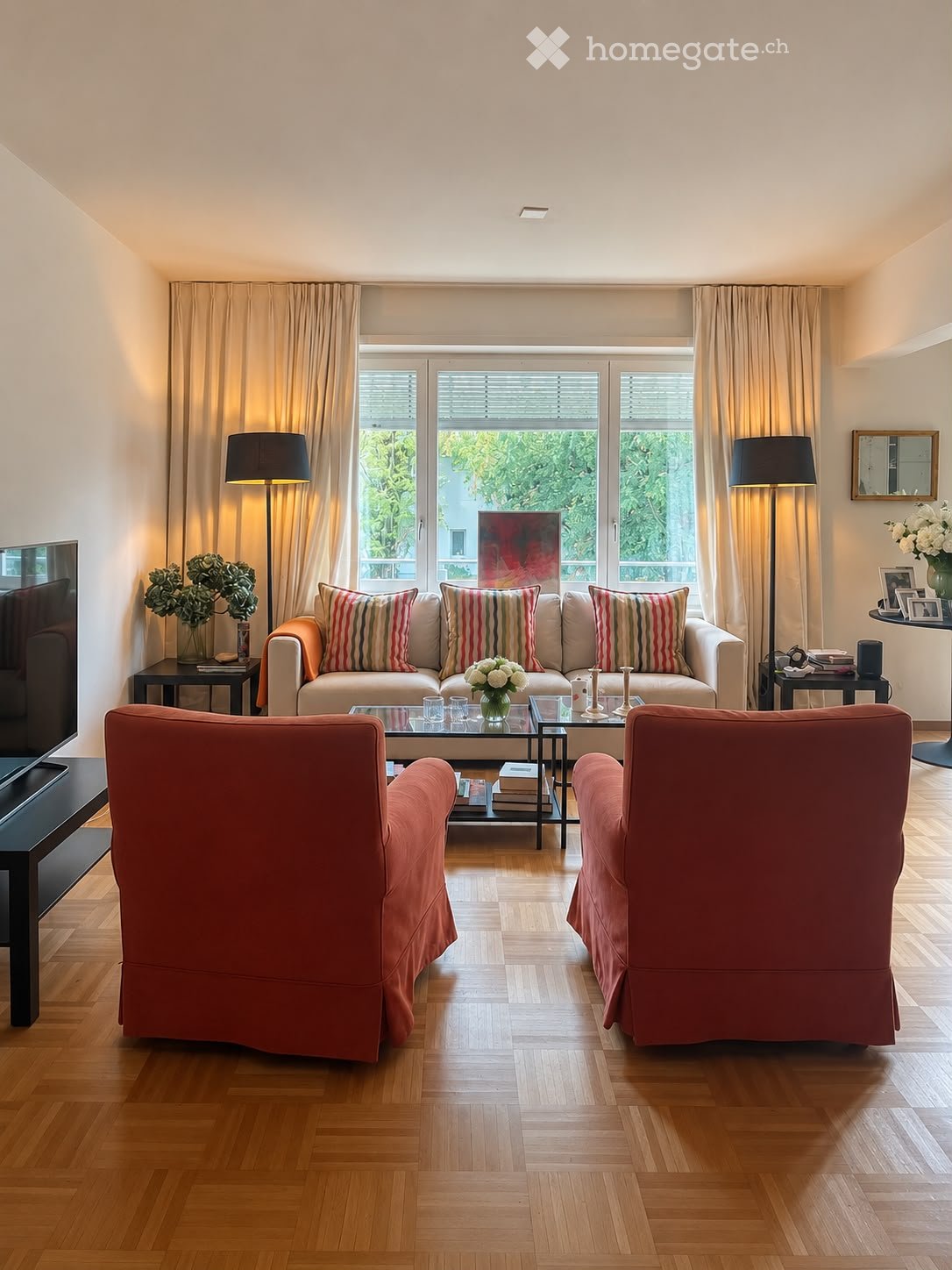Modern living room with light-colored sofa, striped cushions, two armchairs, coffee table, side tables, floor lamps, and decorative vases.