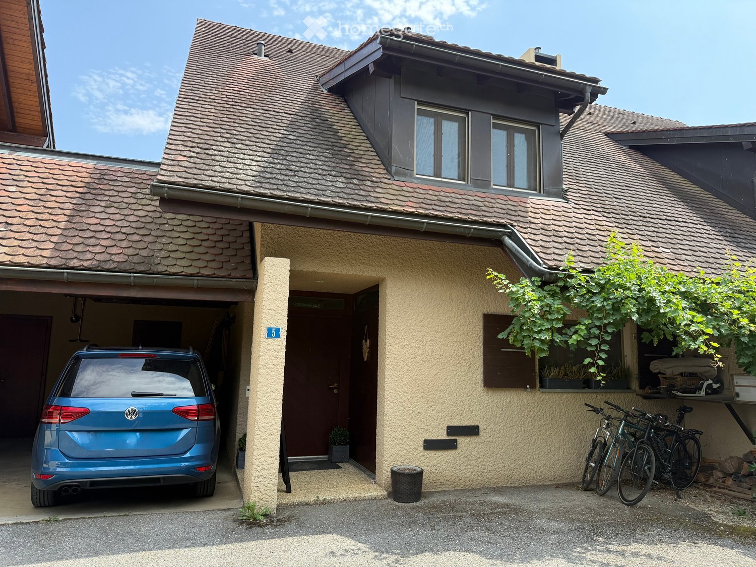 Two-story house with a tiled roof, beige exterior, garage, and bicycles parked outside.