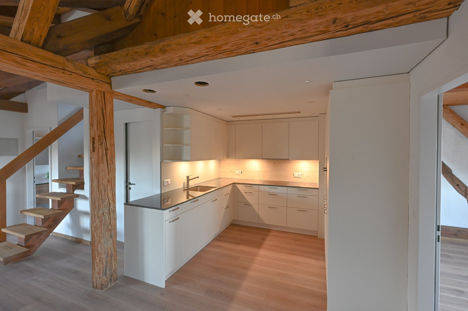 Modern kitchen with white cabinets, a central island, and a wooden staircase leading to an upper level.