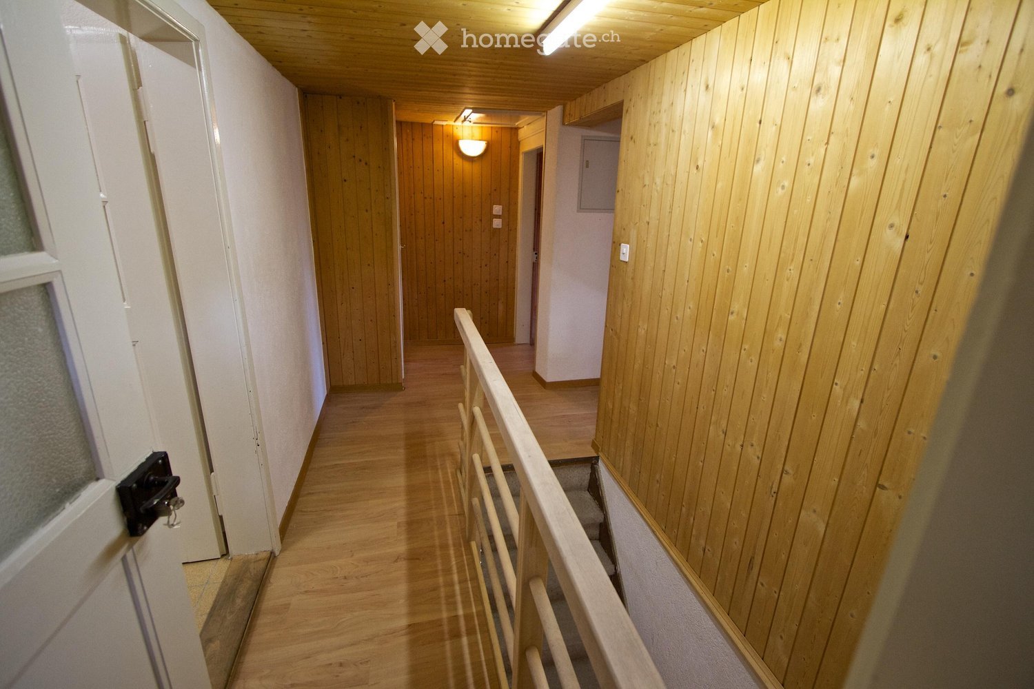 Wooden hallway with a staircase, wooden walls, and a railing leading to another area.