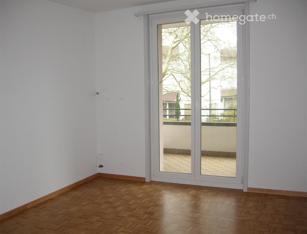 Empty room with wooden flooring, white walls, and a large sliding glass door leading to a balcony.