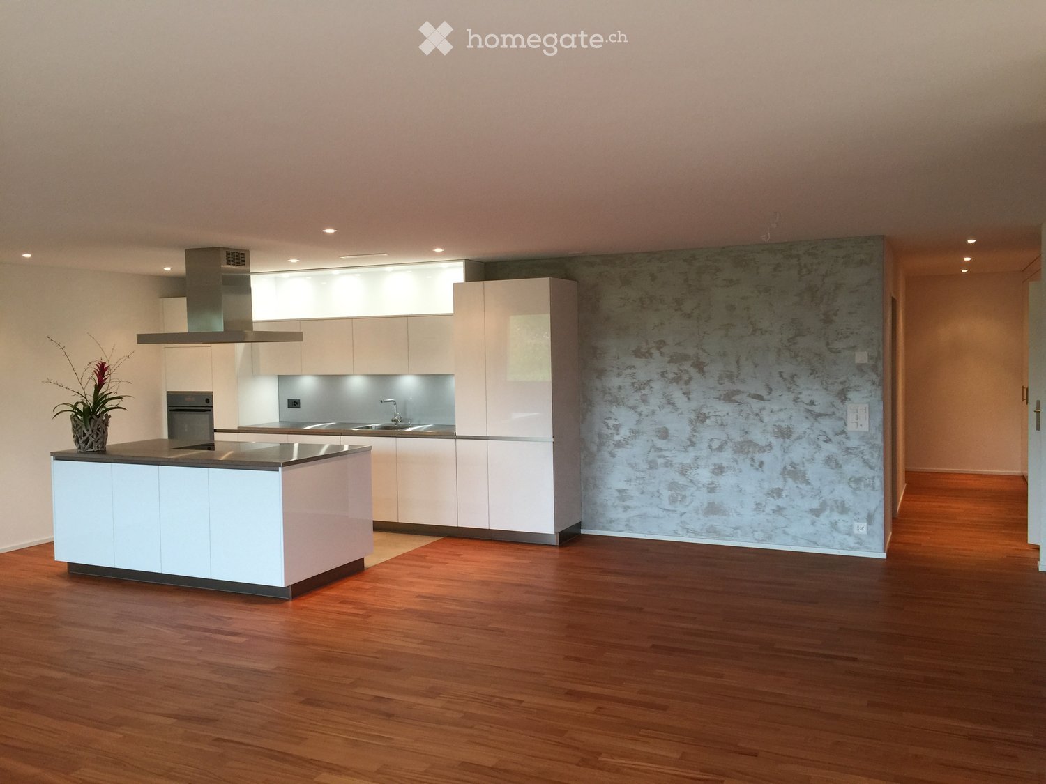 Modern kitchen with white cabinets, a central island, stainless steel appliances, and a textured wall.