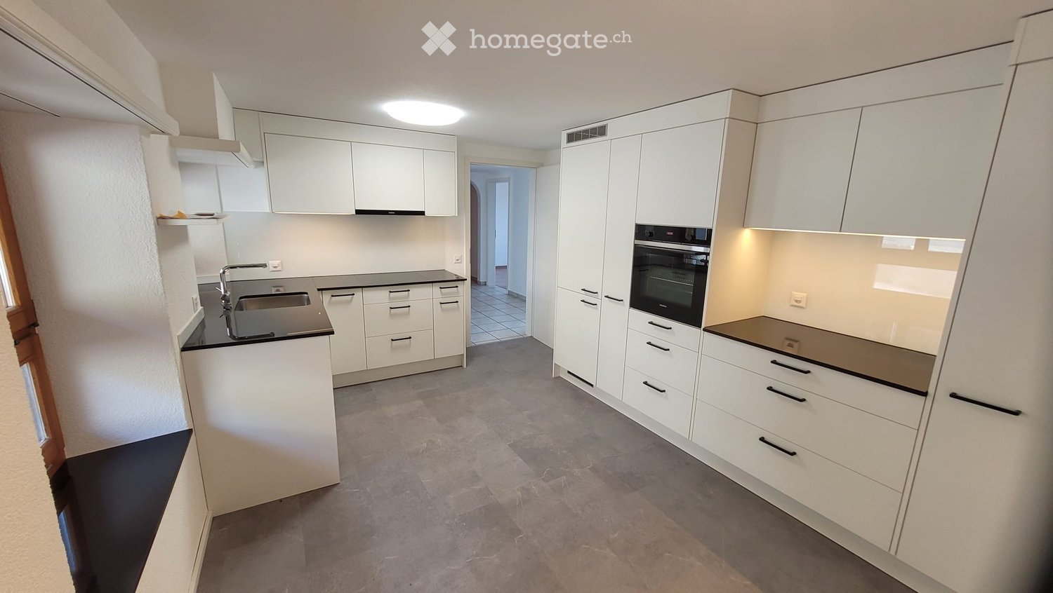 Modern kitchen with white cabinets, black countertops, a sink, and an oven. The space is well-lit with a circular ceiling light and has a clean, minimalist design.
