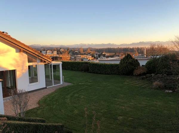 Well-maintained garden with a neatly trimmed lawn, surrounding hedges, and a view of a distant mountain range and suburban neighborhood.