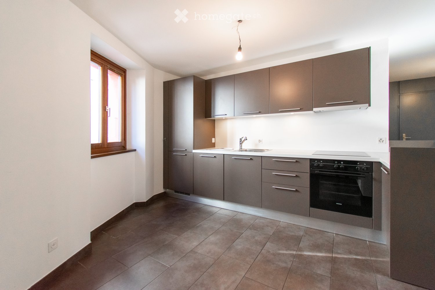 Modern kitchen with dark grey cabinets, a sink, and an oven, featuring tiled flooring and a window on the left side.
