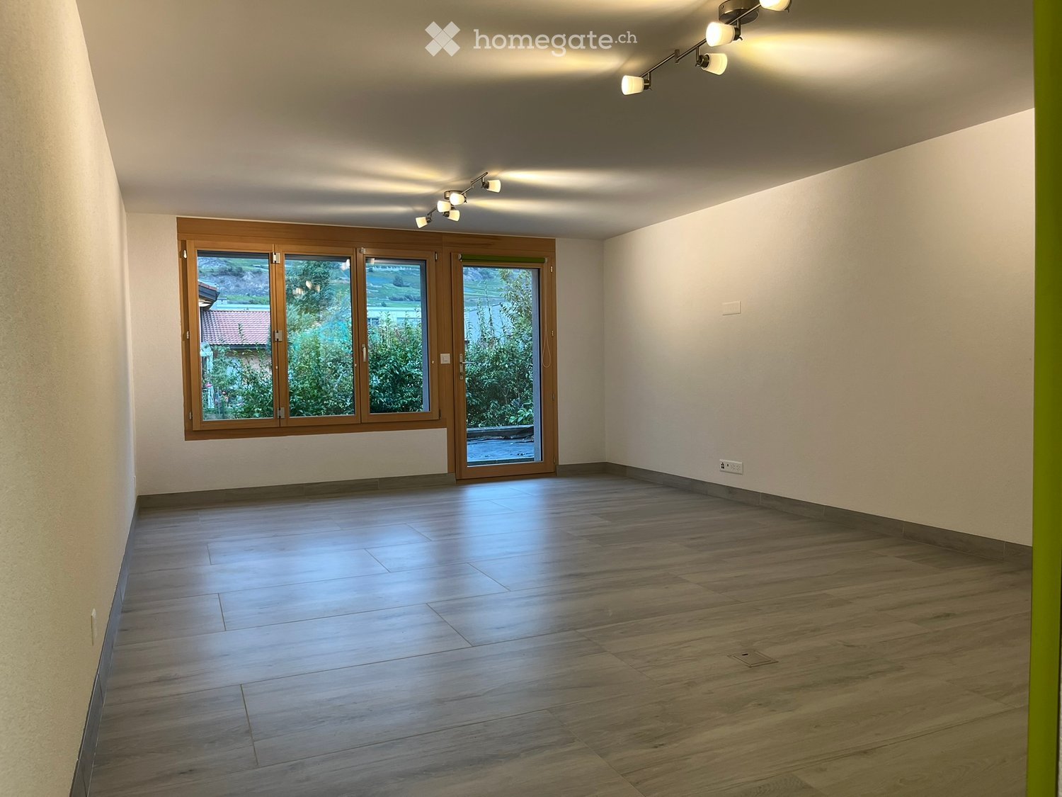 Empty room with wooden flooring, large windows, and recessed lighting. No furniture or equipment present.